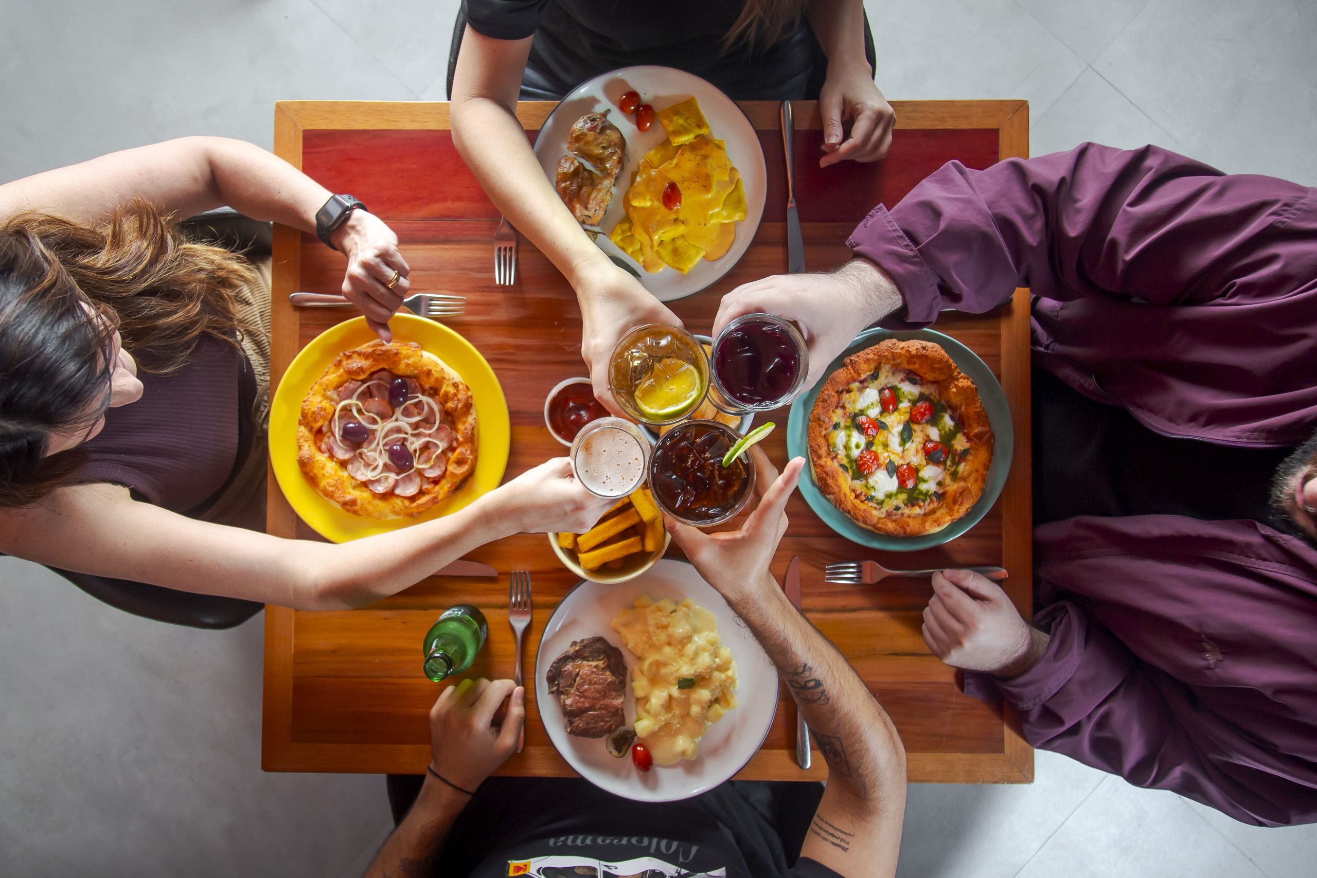 Mesa farta com pessoas brindando a felicidade de saborear pratos autênticos e saborosos